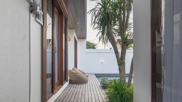 A narrow wooden deck with a sliding glass door, a beige bean bag chair, and a small palm tree. - Cypress Villa (Ungasan)