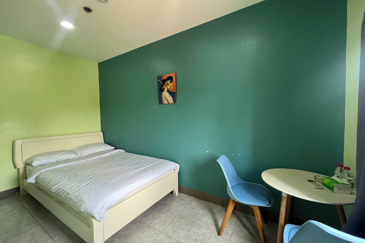 Ein Zimmer mit einem Bett, zwei Stühlen, einem kleinen Tisch und einem Bild an der Wand.