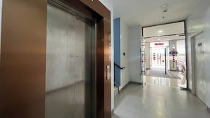 A hallway with a closed elevator door, a blue wall, and a visible entrance to a shop. - Qingqing Hotel Pasay Manila near MOA (Pasay)