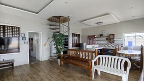 A spacious living area with a wooden floor, a wooden bench, a white plastic bench, a staircase with a metal railing, and a kitchen area with a water dispenser. - Sea Breeze Beachfront Villa Cebu (Argao)