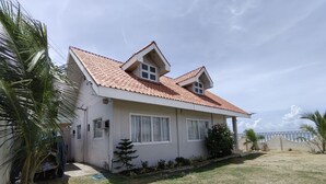 A two-story house with a tiled roof, white exterior walls, and a small front yard with grass and a few plants. - Sea Breeze Beachfront Villa Cebu (Argao)