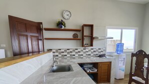 A kitchen with a marble countertop, a sink, wooden cabinets, a clock, a water dispenser, and a window. - Sea Breeze Beachfront Villa Cebu (Argao)