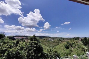 A view of a lush green landscape with scattered buildings in the distance under a clear blue sky with clouds.