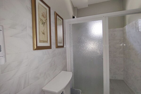 A bathroom with a white toilet, a shower with a glass door, and two framed botanical prints on the wall. - Tampus Staycation Rental Cebu (Talisay)