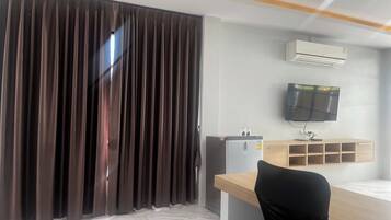A hotel room with a large window, a desk with a chair, an air conditioner, a television, and a minibar.