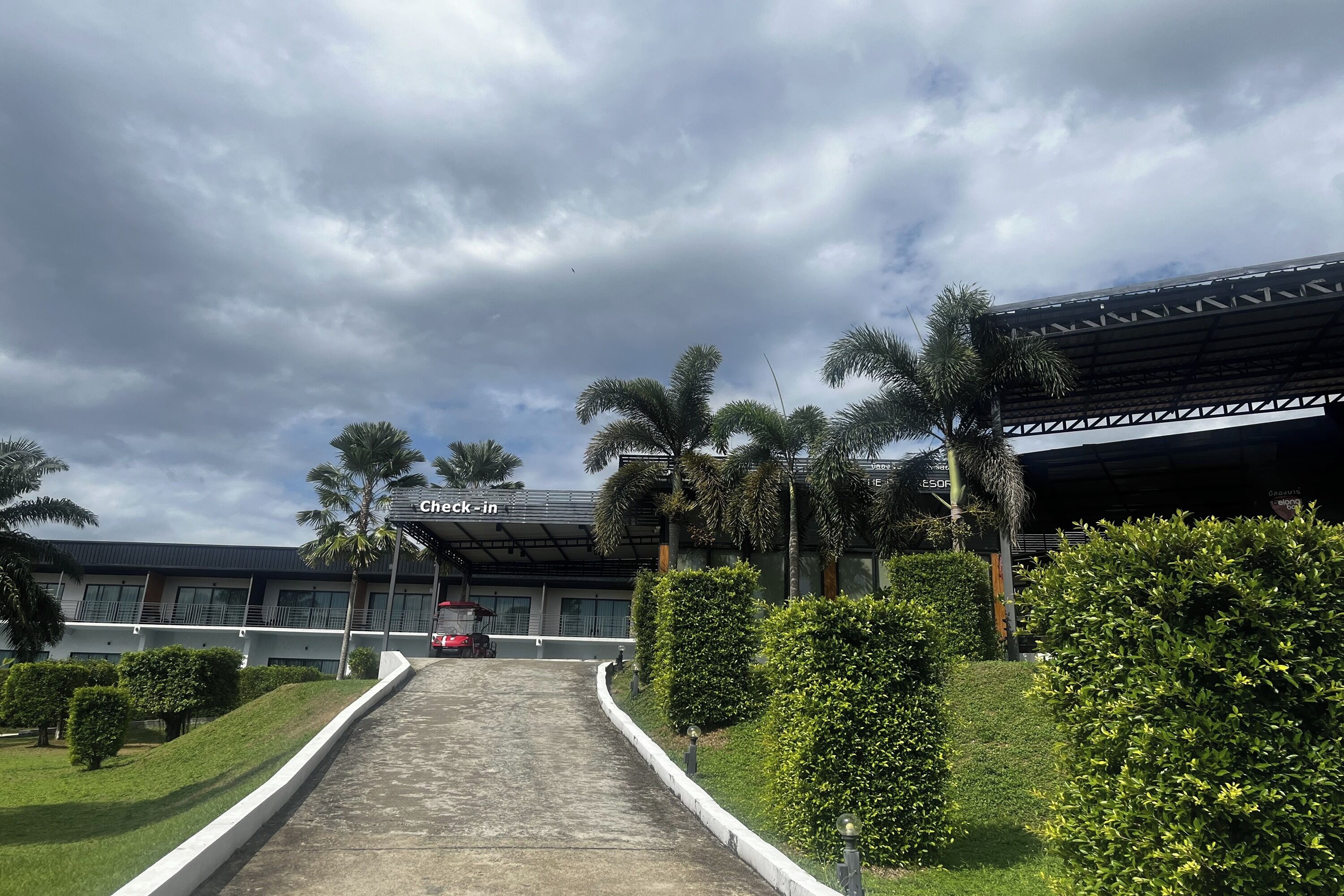 A pathway leading to a building with a 'Check-in' sign, surrounded by greenery and palm trees.