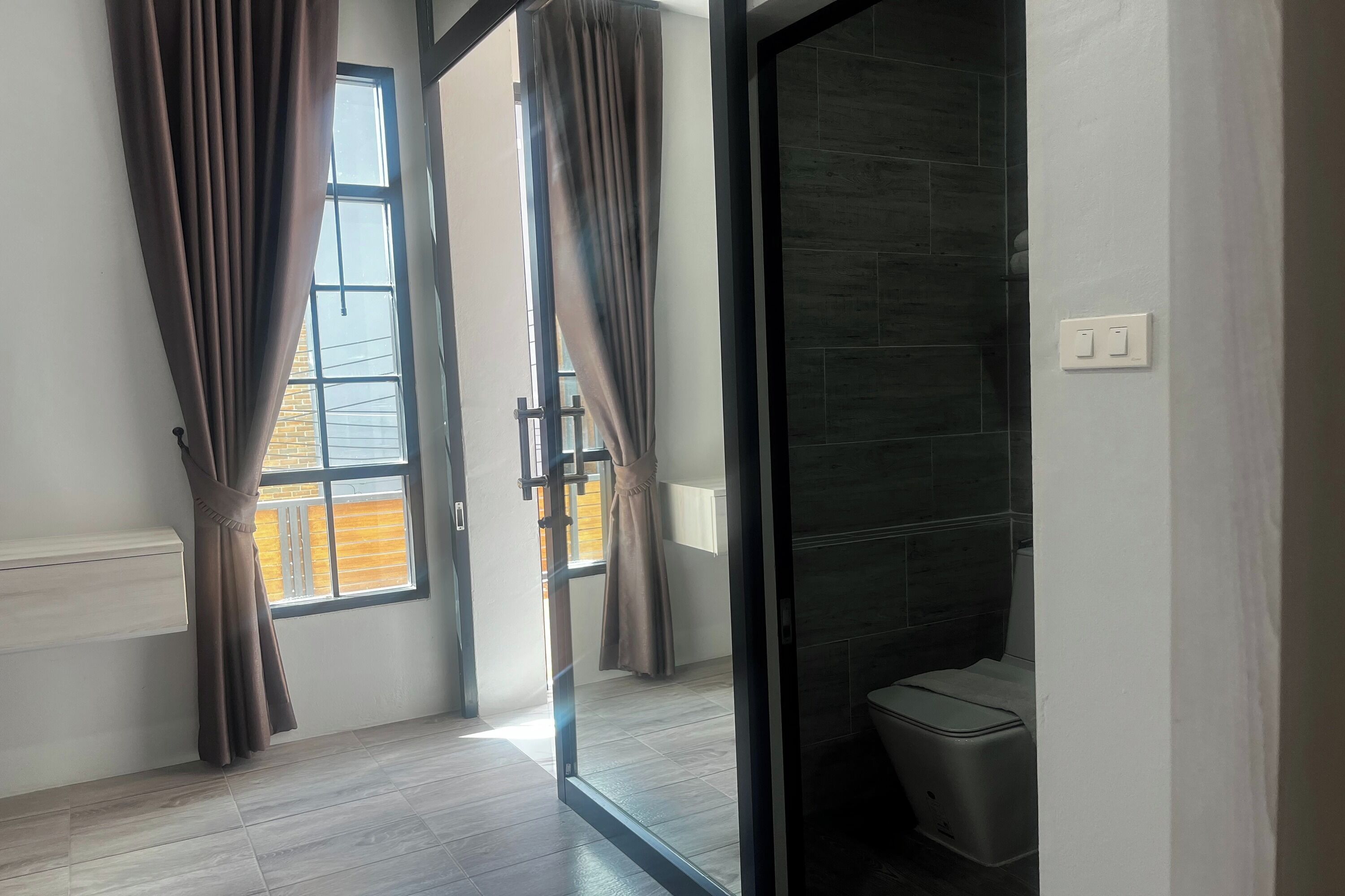 A modern room with a sliding glass door leading to a balcony, a toilet, and a wall-mounted light switch.