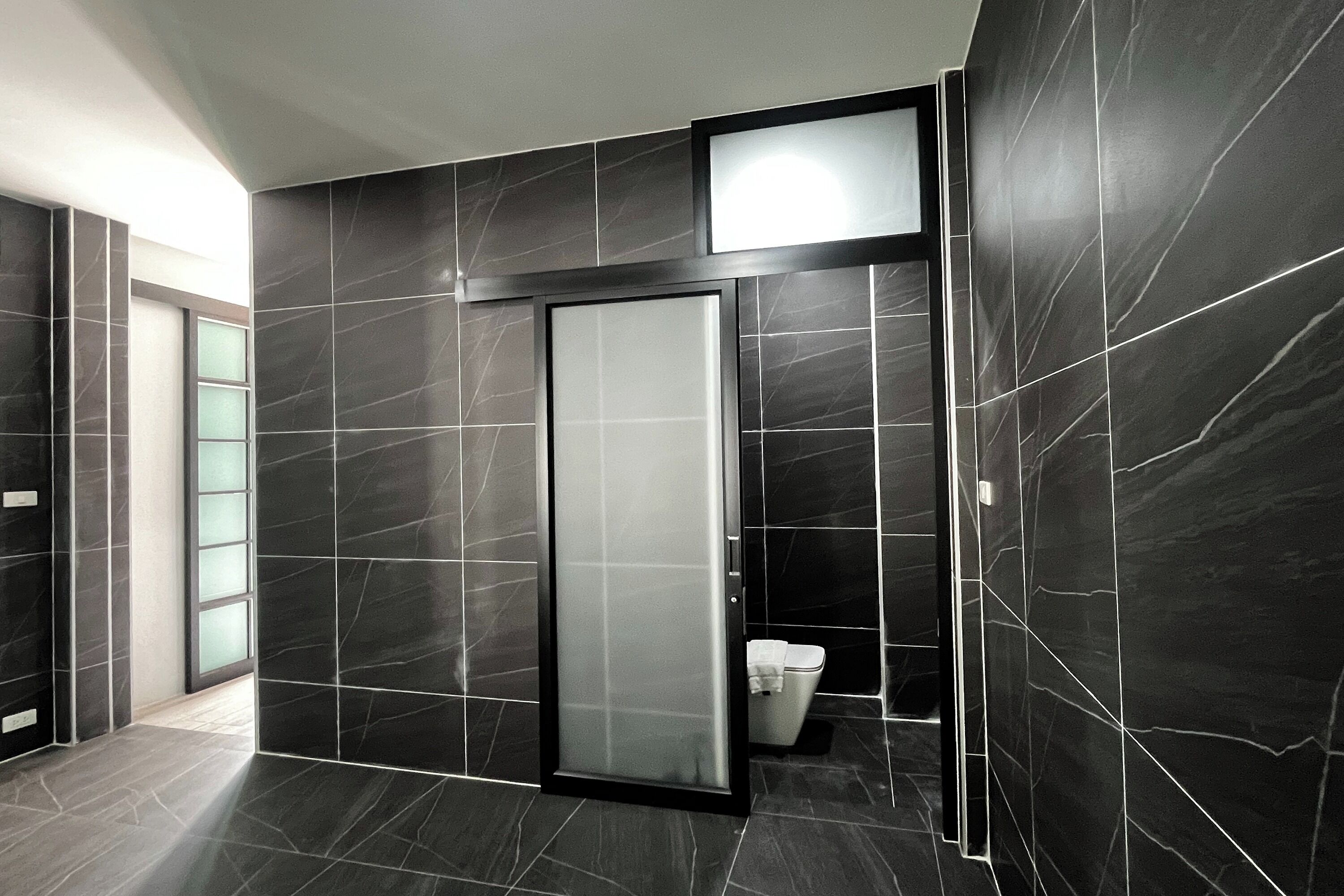 A modern bathroom with dark marble tiles, a glass shower enclosure, and a toilet.