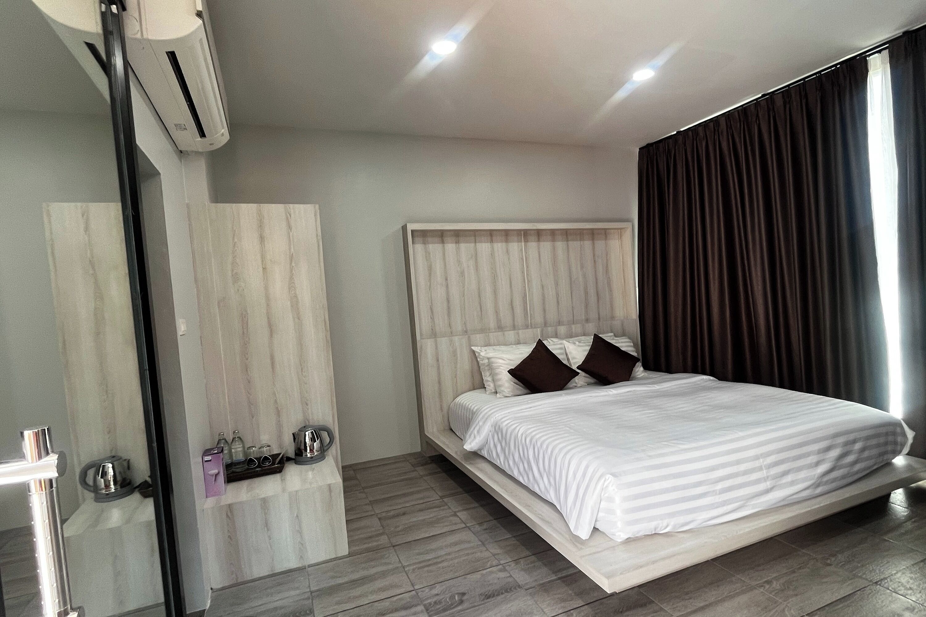 Una habitación de hotel moderna con una cama grande, un armario empotrado, un espejo y una pequeña estantería con artículos de aseo.