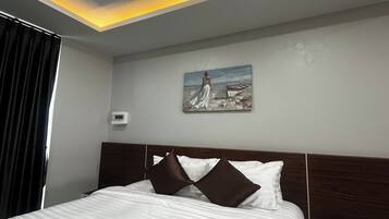 Habitación de hotel con una cama, dos almohadas, un cuadro de una mujer junto al mar y una lámpara en el techo.