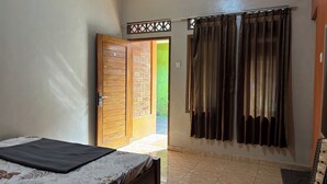 A bedroom with a bed, a window with curtains, a door leading outside, and an air conditioning unit. - Family 24 Hotel near Pantai Cipatujah (Cipatujah)
