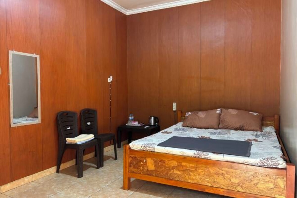 Un dormitorio con una cama de madera, dos sillas, una mesita y un espejo en la pared.