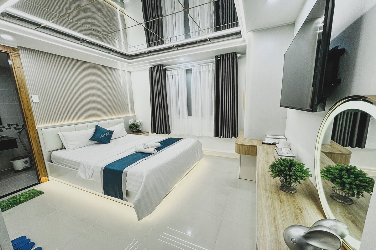 Una habitación de hotel moderna con una cama grande, un espejo, una planta pequeña y un televisor.