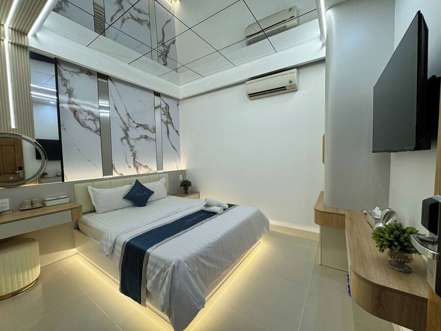 A modern hotel room with a bed, bedside table, and a large mirror.