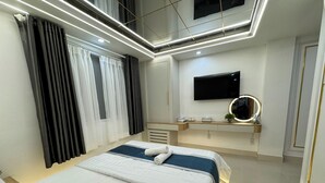 Una habitación de hotel moderna con una cama grande, un televisor de pantalla plana montado en la pared, una mesita de noche con espejo y una ventana con cortinas.
