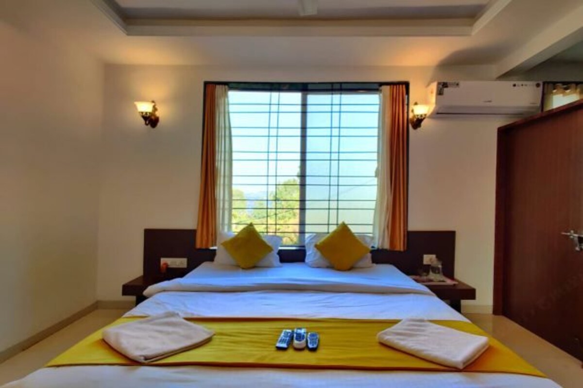Habitación de hotel con una cama grande, dos mesitas de noche, una ventana con cortinas y un equipo de aire acondicionado.