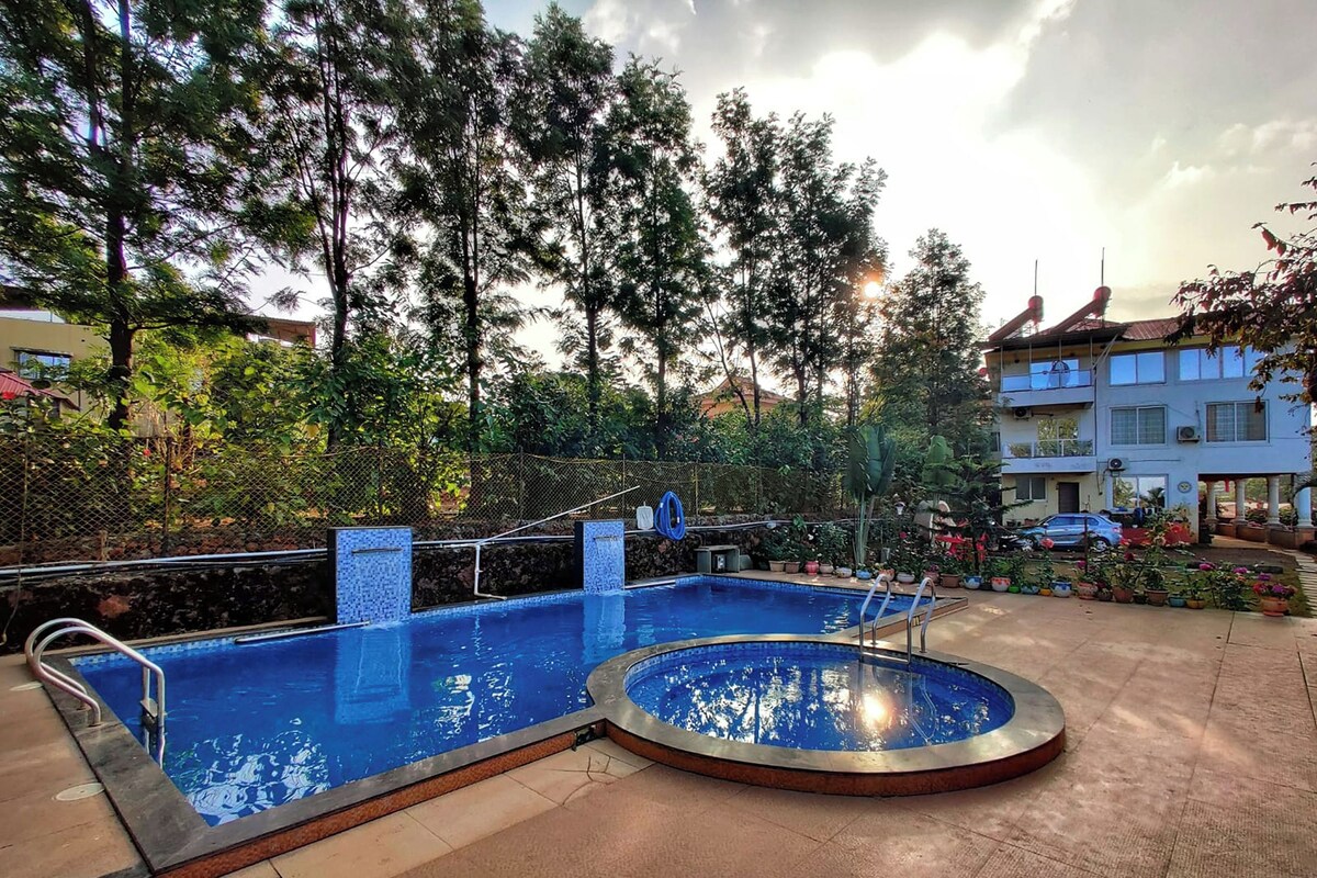 Una piscina al aire libre con solárium de baldosas, rodeada de árboles y un edificio.