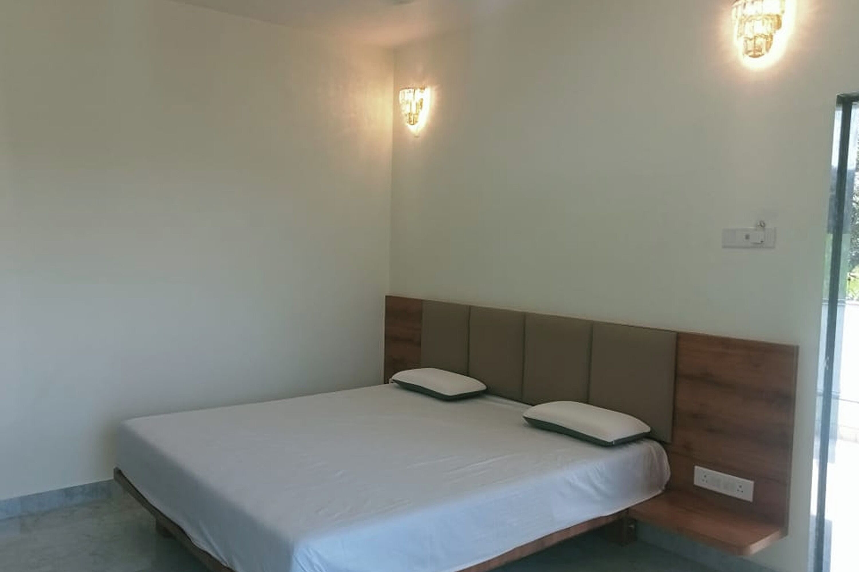 A single bed with a wooden headboard, two wall-mounted light fixtures, and a power outlet on the wall.