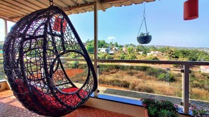 Una silla colgante con un cojín rojo en un balcón con vista a una zona residencial.