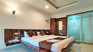Habitación de hotel moderna con una cama grande, cabecera de madera, mesitas de noche con cristalería y un ventanal corredero que da a un balcón.