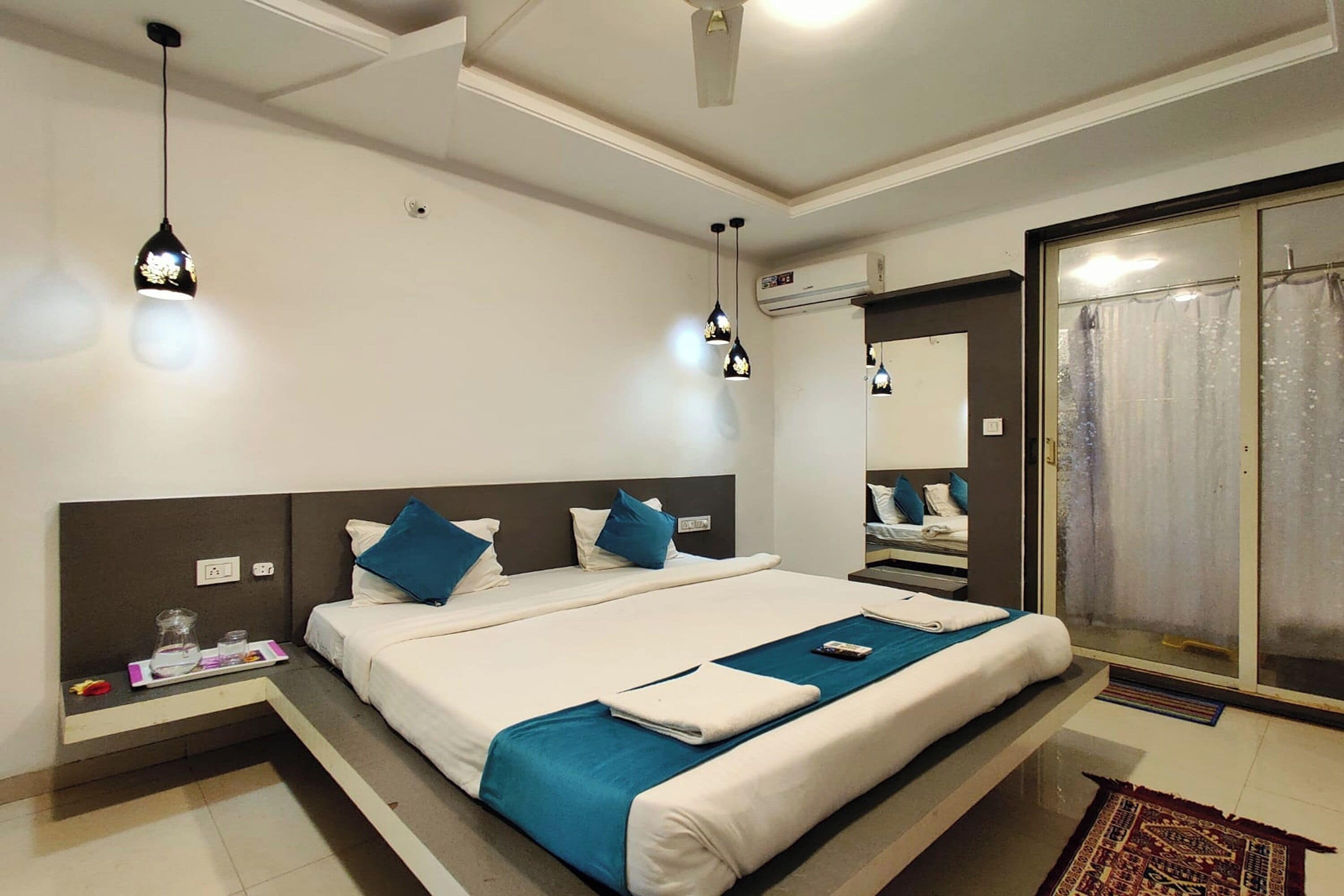 Habitación de hotel con una cama grande, mesitas de noche, un espejo y una puerta de cristal corredera que da a un balcón.