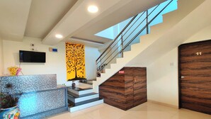 Un área de recepción moderna con una escalera, un televisor de pantalla plana y un panel decorativo en la pared.