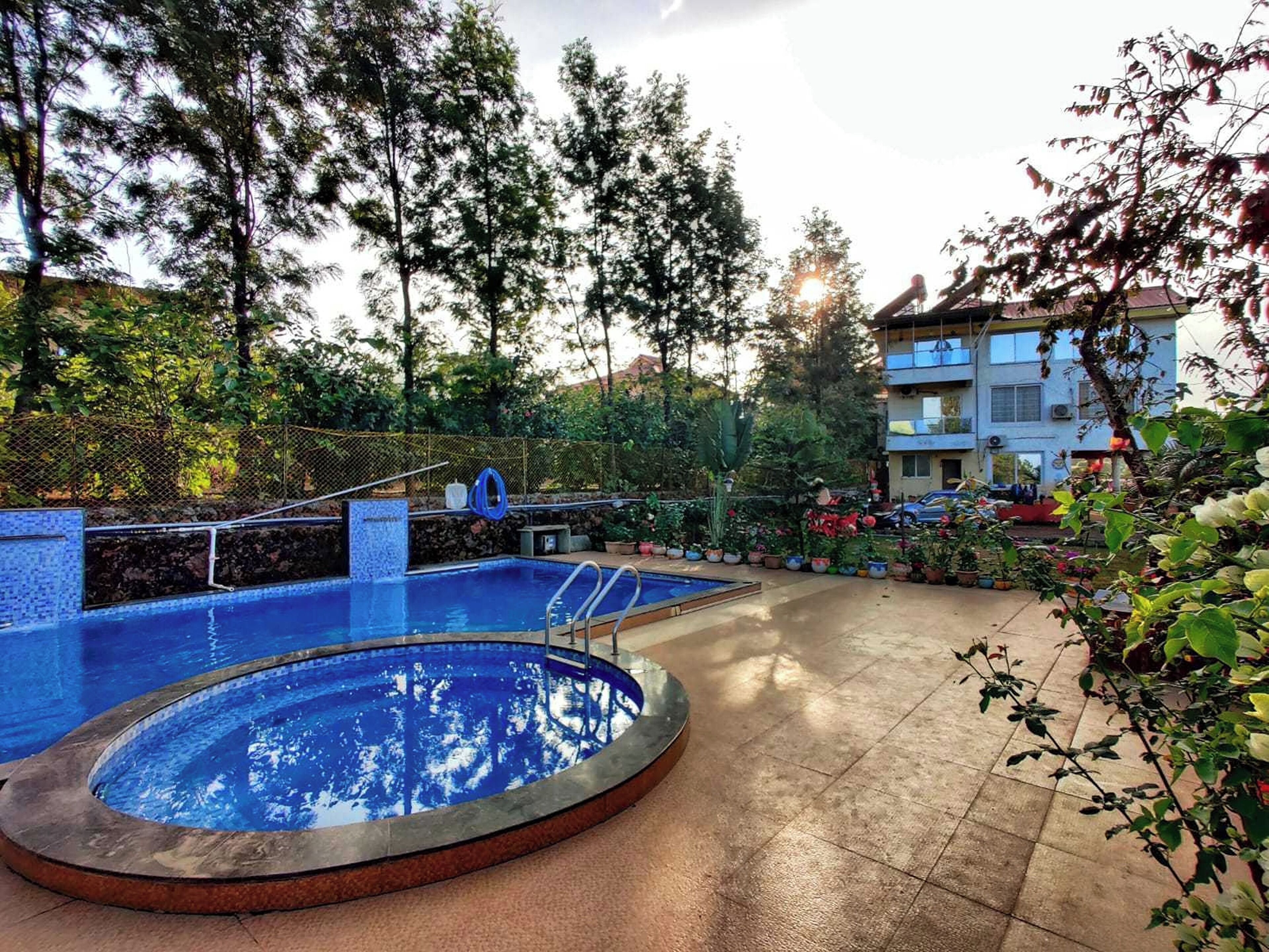 A swimming pool with a tiled edge, surrounded by a garden with various plants and a fence.