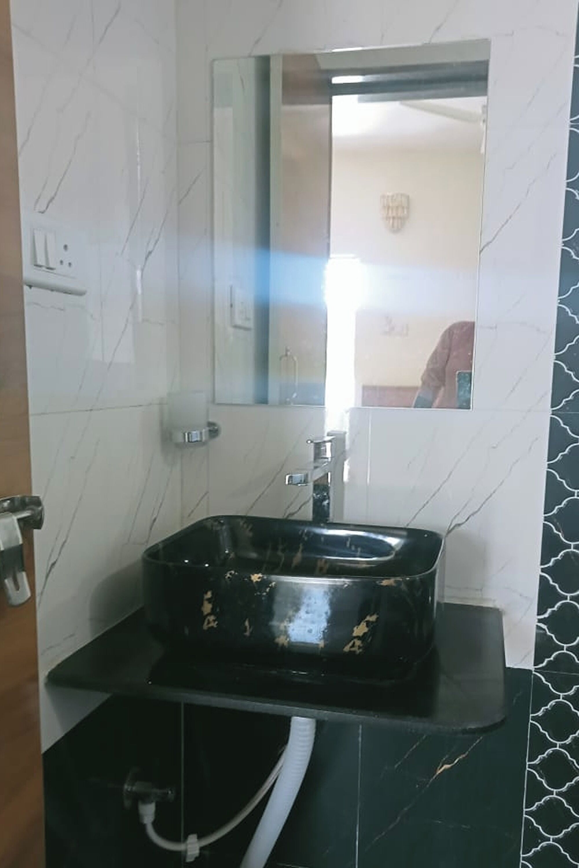 A bathroom with a black sink, white marble walls, and a mirror.