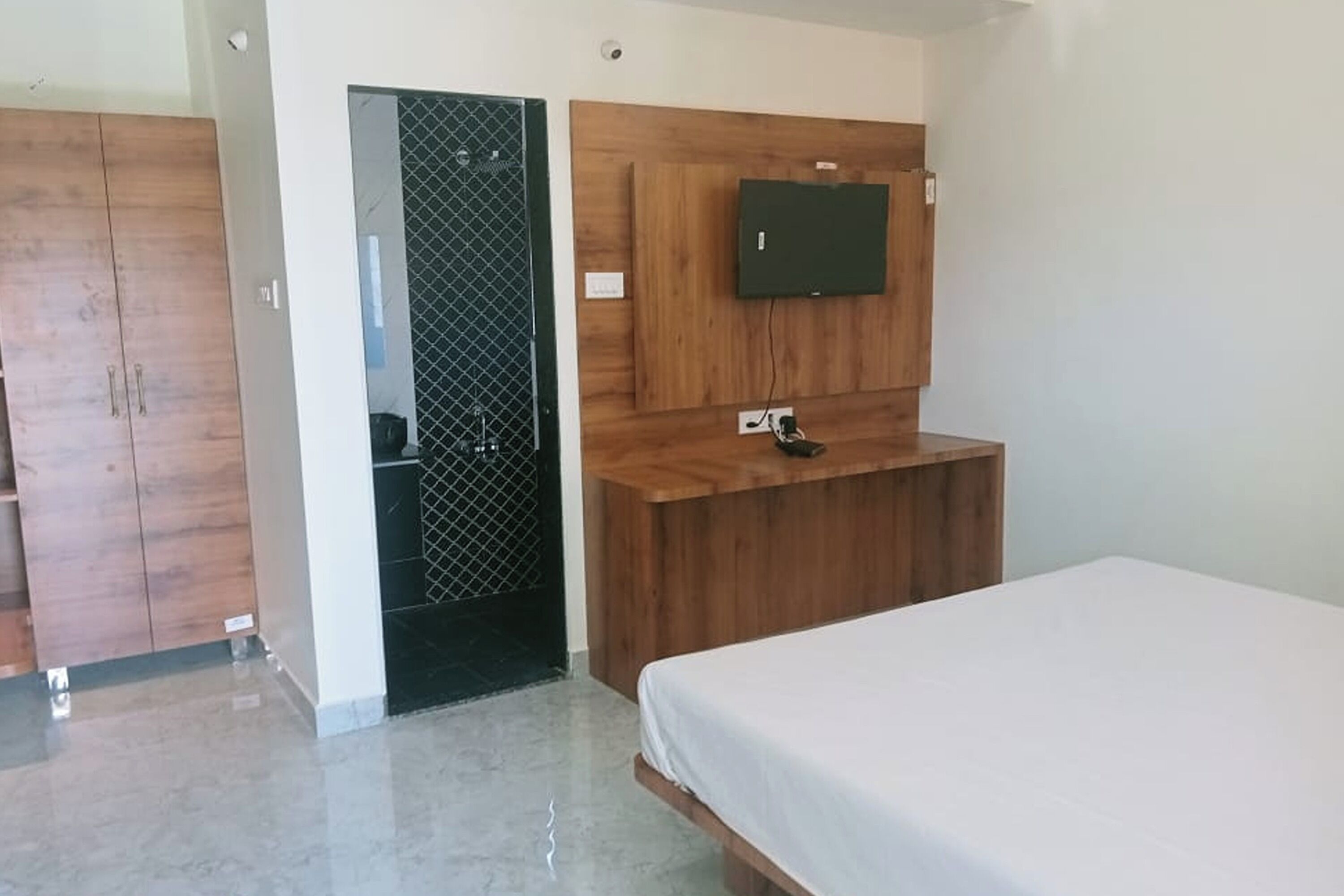 A bedroom with a bed, a wooden wardrobe, a TV mounted on a wooden panel, and a small desk.