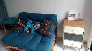 Une pièce avec un canapé de couleur turquoise, des coussins à motifs, une petite table d’appoint en bois ornée d’un objet décoratif et un miroir fixé au mur.