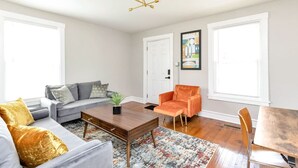 Ein Wohnzimmer mit grauem Sofa, einem orangefarbenen Sessel, einem Holztisch und einem Bild an der Wand.