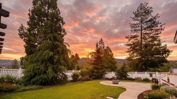 A well-maintained backyard with a curved pathway, surrounded by mature trees and a white fence. - Spacious Yosemite Lodge –Arcades + EV Charger + 3B2B + Private 1 Acre +Game Room (Oakhurst)