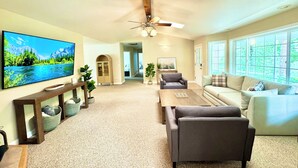 A spacious living room with a flat-screen TV, a ceiling fan, a large window, and a cozy seating area. - Spacious Yosemite Lodge –Arcades + EV Charger + 3B2B + Private 1 Acre +Game Room (Oakhurst)