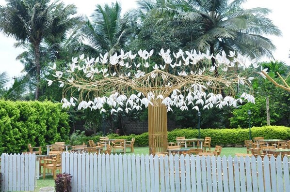 A garden with a white picket fence, wooden chairs, and tables arranged for outdoor dining. - Seed Resort (Shrirangapattana)