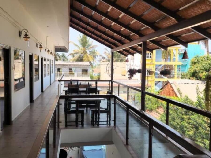 A balcony with tables and chairs, overlooking a lush green area with buildings in the background.