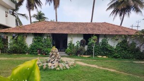 A house with a tiled roof, surrounded by a well-maintained lawn and various plants. - Seed Resort (Shrirangapattana)