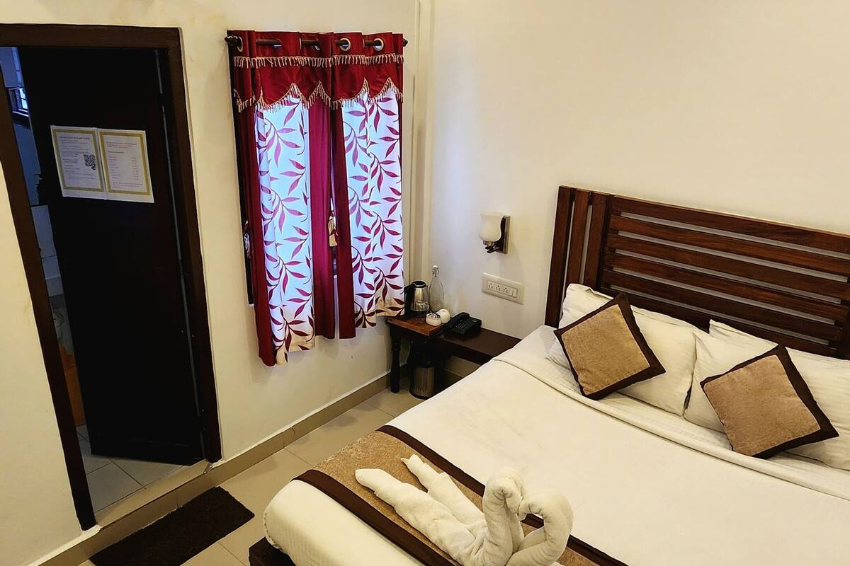 A hotel room with a bed, a bedside table with a lamp, a wall-mounted air conditioner, and a ceiling fan.