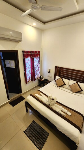 A hotel room with a bed, a bedside table with a lamp, a wall-mounted air conditioner, and a ceiling fan. - Seed Resort (Shrirangapattana)