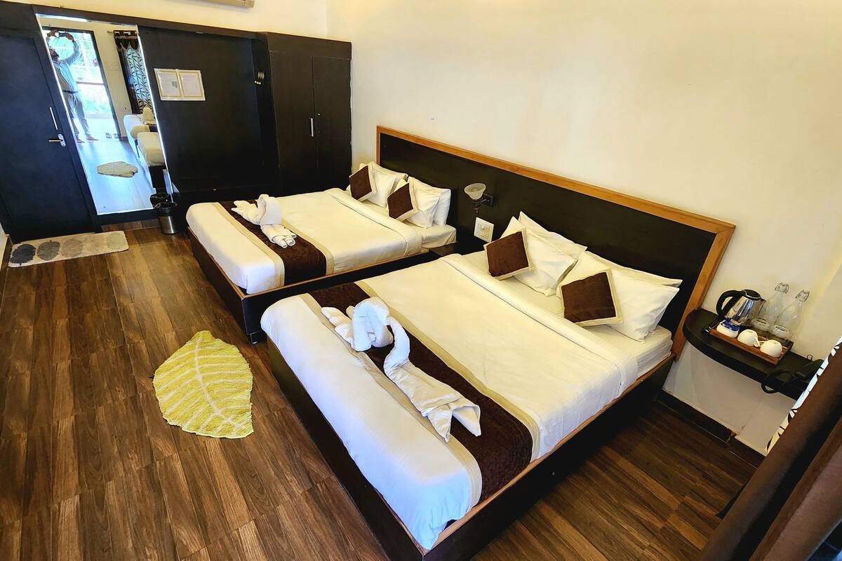 A hotel room with two beds, a wooden floor, a small table with a tray, and a door leading to the outside.