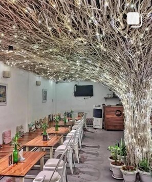 A conference room with long tables and chairs, a projector screen, and a decorative tree-like structure with lights. - Seed Resort (Shrirangapattana)