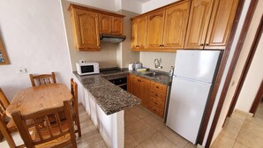 Une cuisine de taille réduite, dotée de meubles en bois, d’un four à micro-ondes, d’une cuisinière, d’un évier et d’un réfrigérateur.