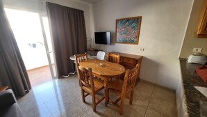 Un coin repas avec une table et des chaises en bois, un téléviseur fixé au mur et un tableau qui le surplombe.