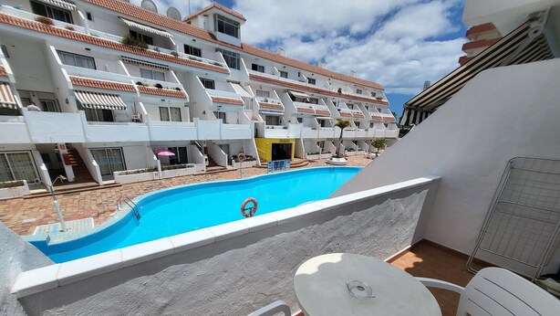 Un balcon avec une piscine, des chaises blanches et une table.