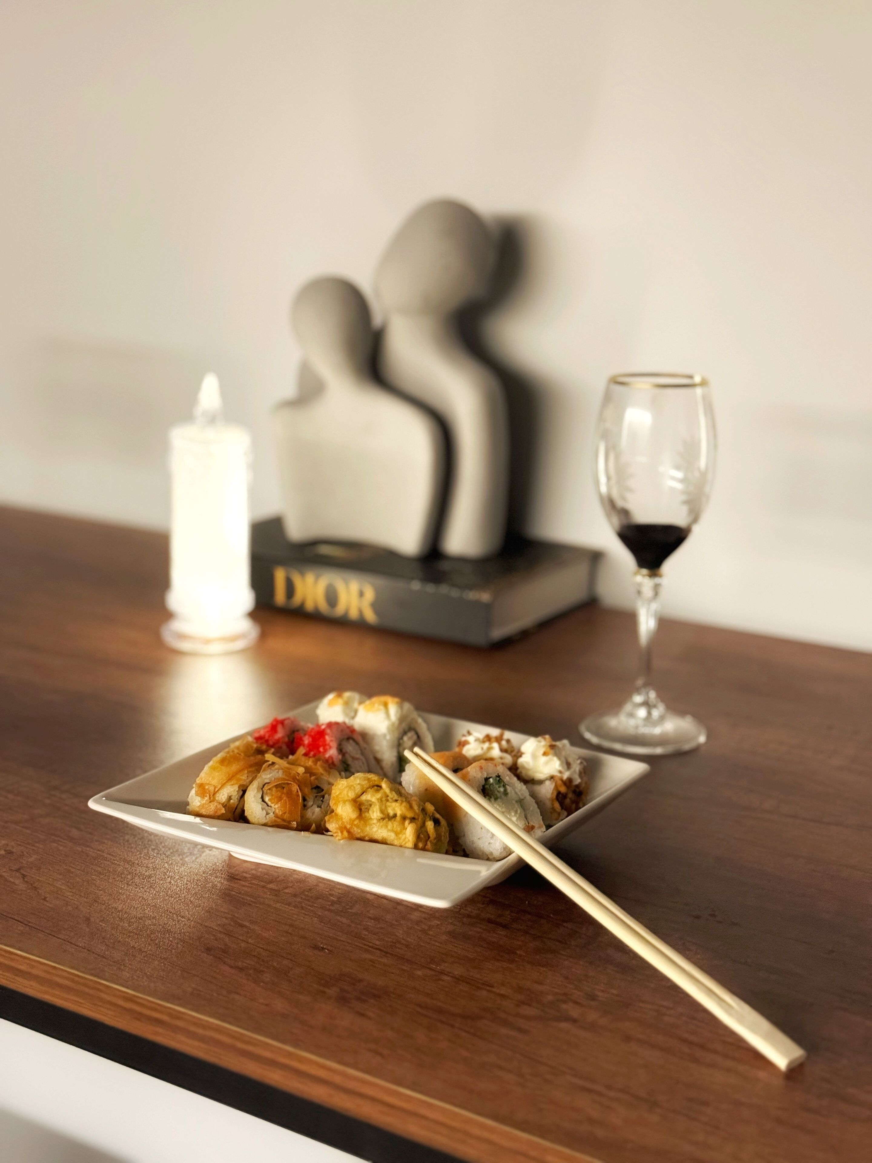 Lautasella sushi-annos, puisella pöydällä syömäpuikot, kynttilä ja lasi viiniä.