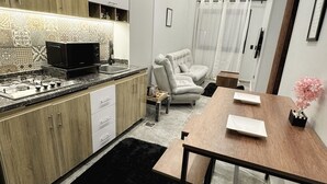 A modern kitchen with a microwave, stove, and wooden cabinets. There is a dining area with a table and chairs, and a black rug on the floor. - Private Jacuzzi 1BDR suite with garden at New Cairo (New Cairo City)