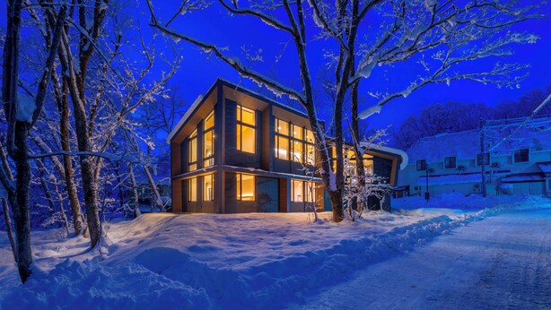 A modern two-story house with large windows and a snow-covered landscape at night. - Villa Lily (Hakuba)