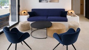 Ein modernes Wohnzimmer mit einem blauen Sofa, zwei blauen Sesseln, einem runden Couchtisch und zwei Beistelltischen mit Lampen.