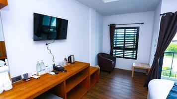 Quarto de hotel com escrivaninha de madeira, televisão de tela plana, uma cadeira, cama e janela com persianas.