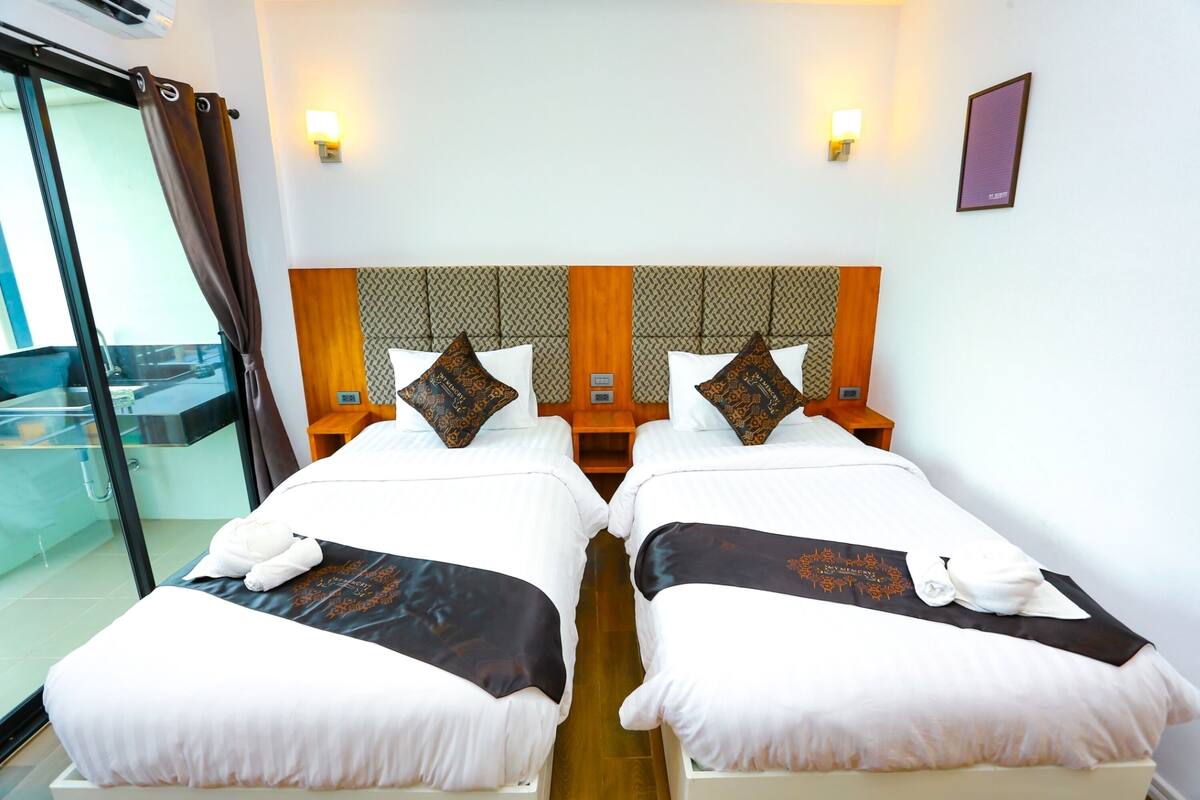A hotel room with two beds, each with white bedding and decorative pillows, a wooden headboard, and a glass partition.
