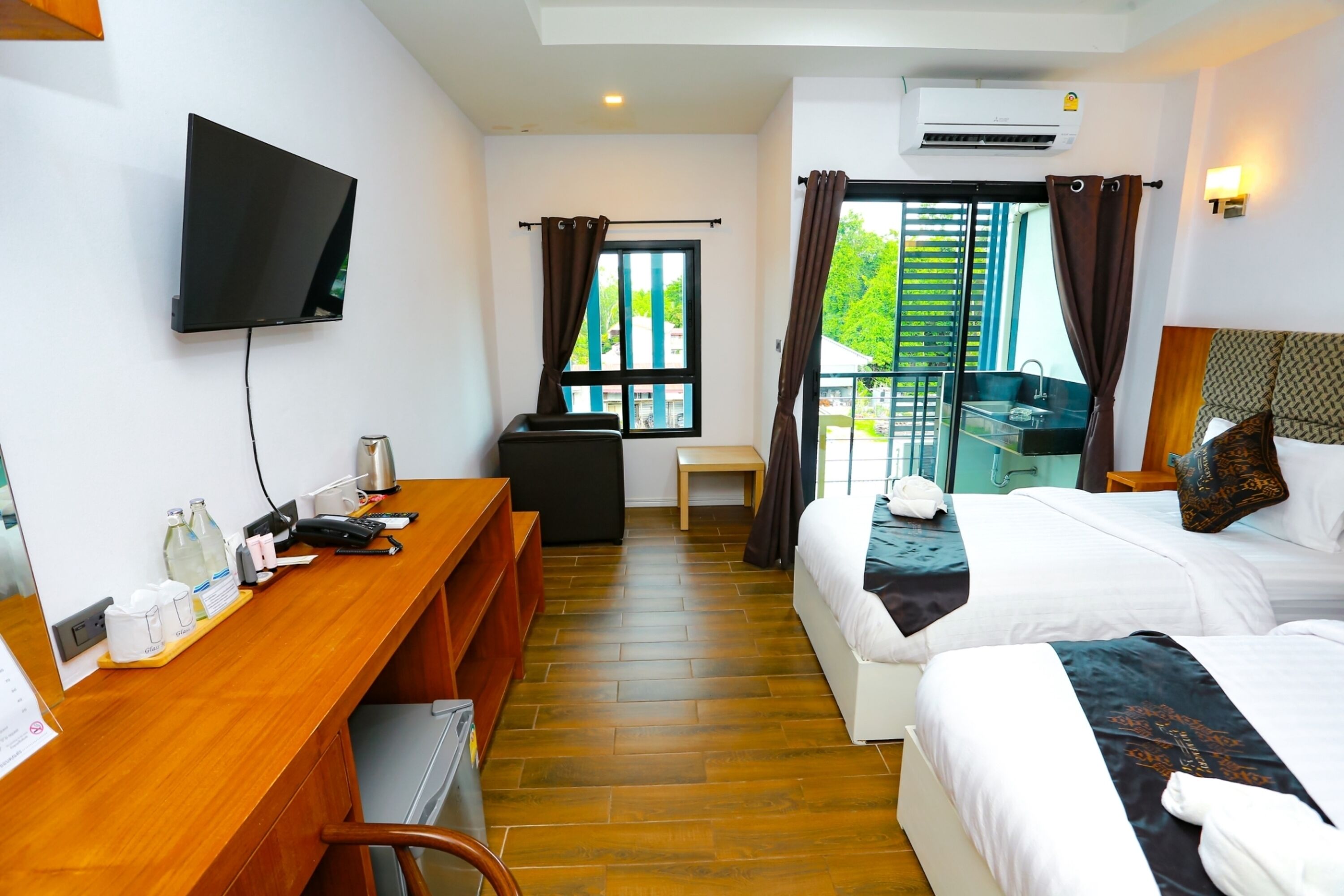 Habitación de hotel con escritorio de madera, televisor de pantalla plana, cama con ropa blanca y balcón con vistas a zonas verdes.